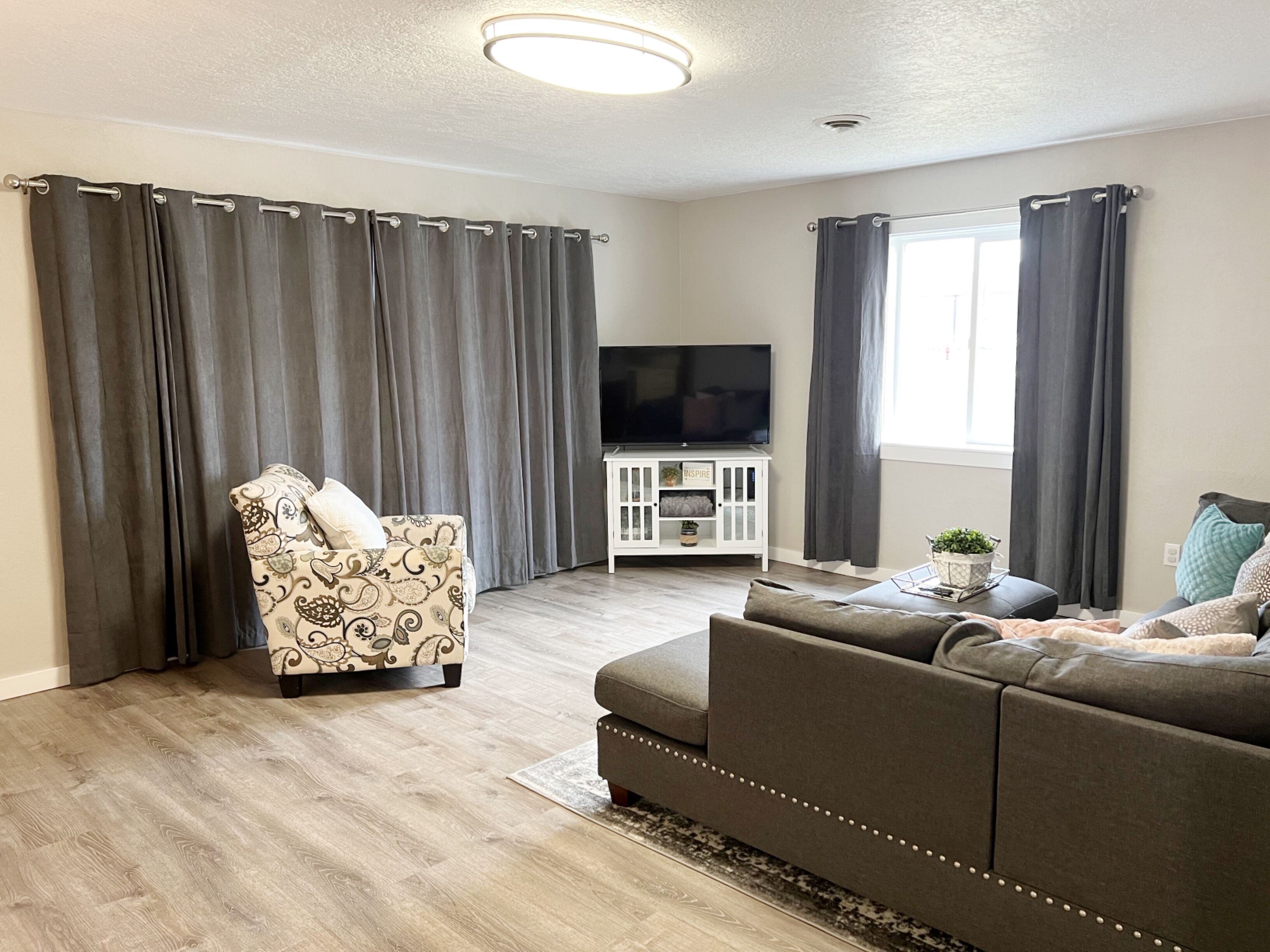 Een woonkamer met een bank, een gestreept fauteuil, een tv-meubel en grijze gordijnen.