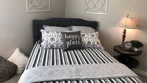 A neatly made bed with striped bedding and decorative pillows, including one with "happy place" text. - *Gorgeous Hideout, Close to everything, 3 bedrooms, fully remodeled!* (Salina)