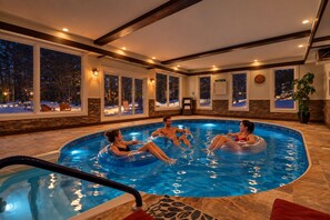 Une piscine intérieure où flottent quatre personnes sur des bouées gonflables, le tout entouré de murs en pierre et de grandes fenêtres.