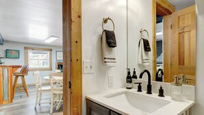 A modern bathroom with a white sink, black faucets, and a large mirror. There are two towels hanging on towel rings, one with a black and white pattern and the other plain white. A glass jar is placed on the sink's edge. - SPLISH SPLASH! Explore Vermont! (Londonderry)