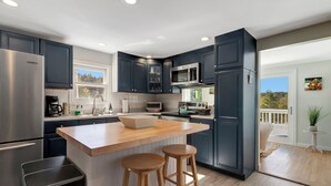A modern kitchen with dark cabinets, stainless steel appliances, a wooden island with stools, and a view of a balcony. - SPLISH SPLASH! Explore Vermont! (Londonderry)