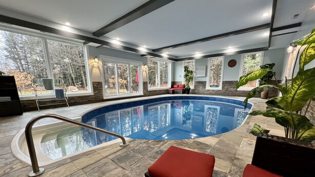 An indoor swimming pool with stone flooring, red cushioned seating, and large windows offering views of trees. - SPLISH SPLASH! Explore Vermont! (Londonderry)