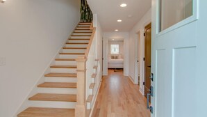 Una escalera con escalones de madera y barandillas blancas que conduce a un dormitorio con cama y ventana.