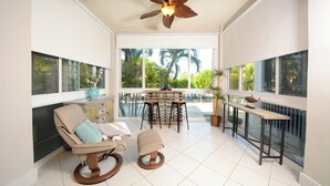 A sunlit room with a chair, a table, and a view of palm trees through large windows. - 207 Mariners Club - Well appointed 3 bedroom, 3 Bath Townhome (Key Largo)