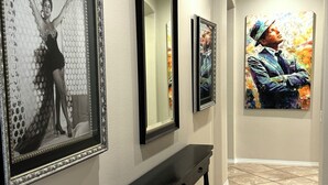 A hallway with framed artwork on the walls, a black console table, and a tiled floor.