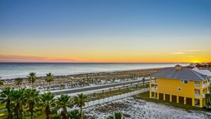 A yellow building with a balcony, located near a beach with palm trees and a road. - P5-0503 Stunning Gulf Front Terrace Sunset Views! (Pensacola Beach)