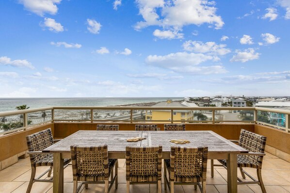 Een houten tafel met geweven stoelen op een balkon met uitzicht op de oceaan.