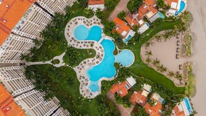 Vista aérea de un complejo turístico con varias piscinas, tumbonas y palmeras.