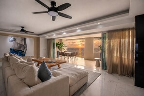A modern living room with a sofa, coffee table, and a ceiling fan. There is a balcony with a view of the sunset. - Gorgeous condo at Marina area , great views , luxury layout, jacuzzi,beach front (Puerto Vallarta)