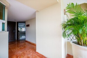 Un couloir avec un sol carrelé, une plante en pot et une porte surmontée d’un portail en métal.