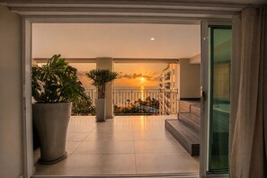 Un balcon offrant une vue sur le coucher de soleil sur l’océan, agrémenté de plantes en pot et donnant sur un espace piscine.