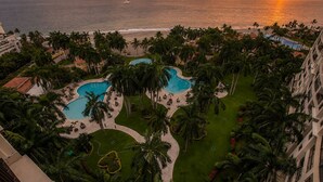 A resort with multiple swimming pools, palm trees, and a view of the ocean at sunset. - Gorgeous condo at Marina area , great views , luxury layout, jacuzzi,beach front (Puerto Vallarta)