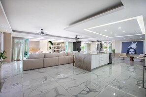 Un salon moderne avec un sol en marbre, un canapé beige, un îlot de cuisine et un coin repas avec des chaises.
