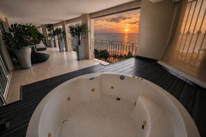 A balcony with a hot tub, potted plants, and a view of the sunset over the sea. - Gorgeous condo at Marina area , great views , luxury layout, jacuzzi,beach front (Puerto Vallarta)