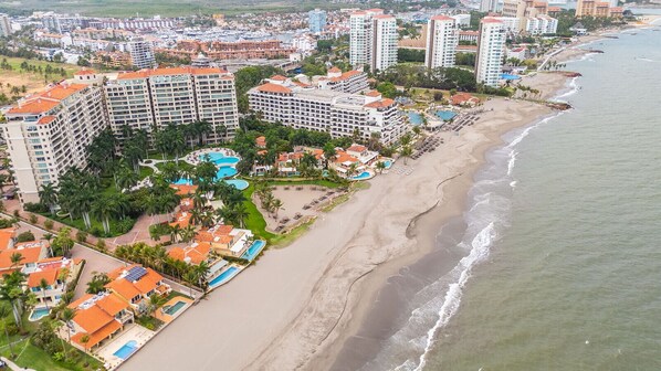 A coastal resort area with multiple high-rise buildings, a sandy beach, and a large swimming pool complex.