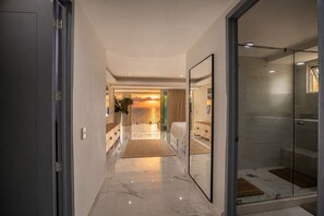 Un couloir d’hôtel moderne avec une douche en verre, un lit et une vue sur le coucher du soleil.