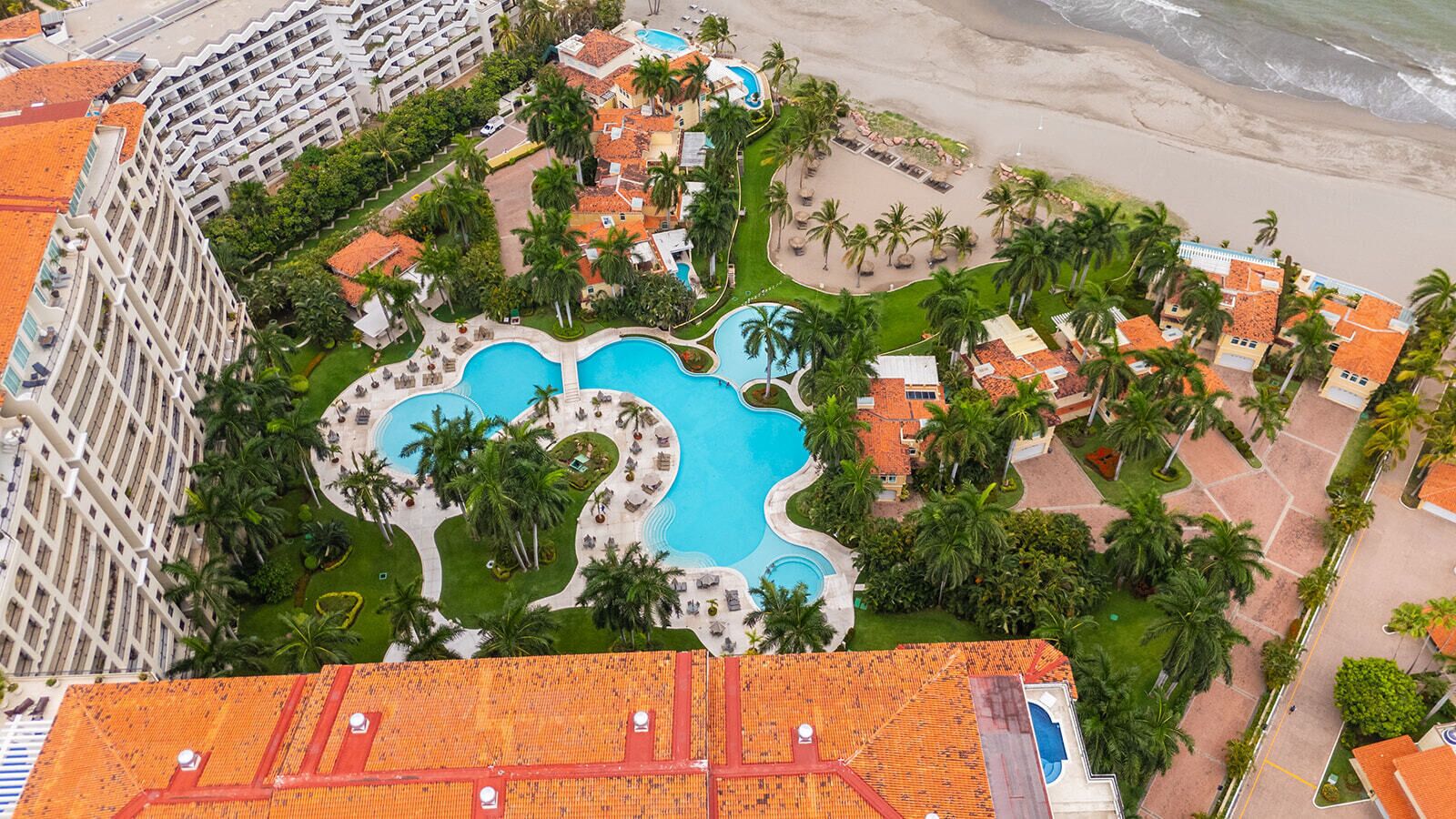 Ein Resort mit mehreren Schwimmbecken, Palmen und direktem Zugang zum Strand.