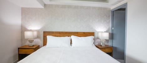 A hotel room with a large bed, two bedside tables with lamps, a wooden headboard, and a patterned wall.