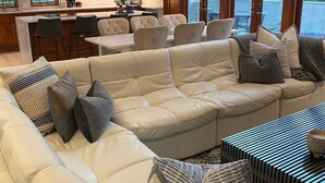 Una sala de estar moderna con un amplio sofá modular, un comedor y una cocina con armarios de madera y un ventanal grande.