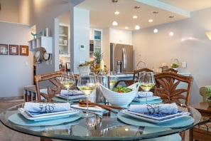 Un moderno comedor con una mesa de vidrio dispuesta para dos, con platos de diseño azul y servilletas blancas.