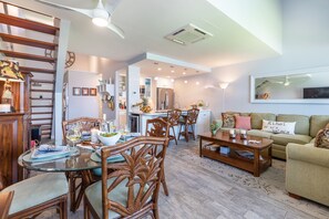 Una cocina moderna con zona de comedor, que incluye una mesa de vidrio, sillas de mimbre y un sofá verde.