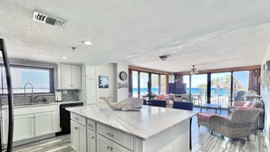 Eine moderne Küche mit einer großen Kochinsel, ein Essbereich mit Meerblick und ein Wohnbereich mit einem Balkon, der auf das Meer hinausblickt.