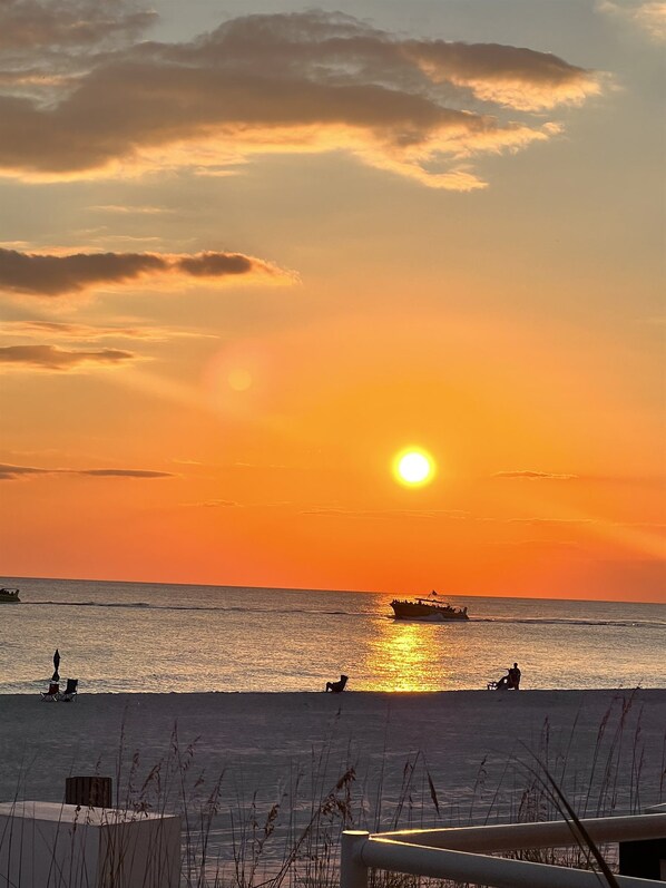 A beach scene with a sunset, boats, and people relaxing on the sand.