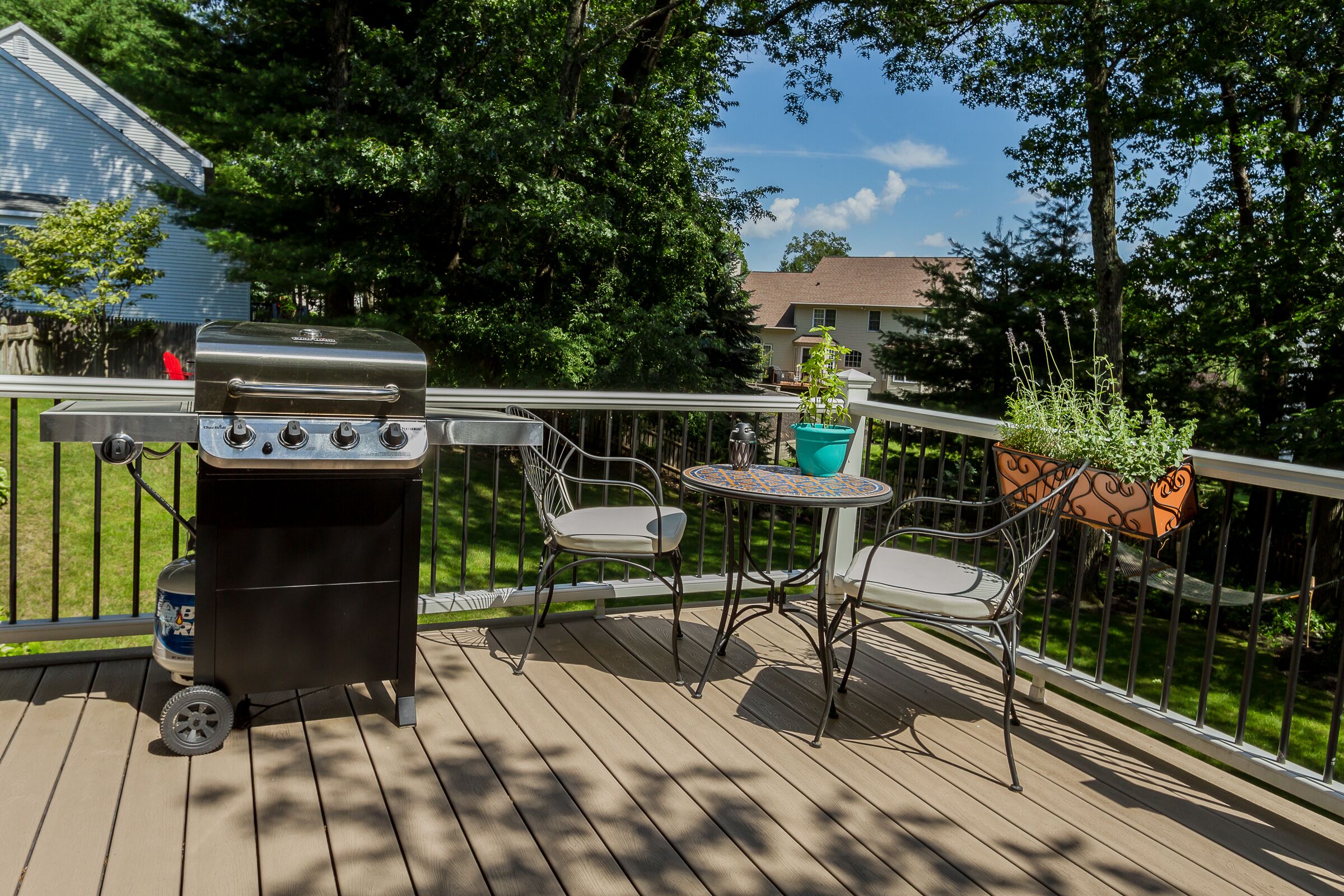 Eine Terrasse mit Grill, zwei Stühlen, einem kleinen Tisch und Topfpflanzen.