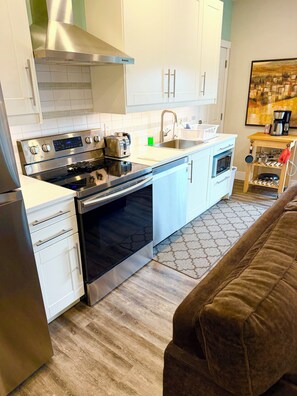 A modern kitchen with stainless steel appliances, white cabinetry, and a wooden coffee table. - Hot Tub (Sept-June), King size bed, AC & Fireplace. (Vernon)