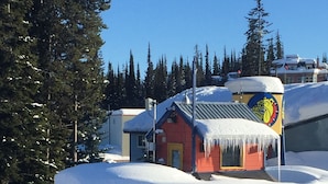 A red building with a snow-covered roof, a ski patrol sign, and a ski rental stand.