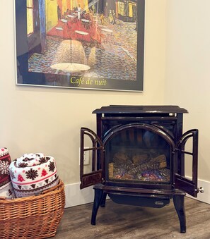 A vintage stove with a glass door, a framed painting above it, and a wicker basket with a patterned blanket on the floor. - Hot Tub (Sept-June), King size bed, AC & Fireplace. (Vernon)