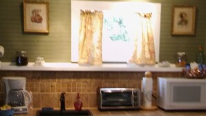 Eine Küche mit Mikrowelle, Toaster und Kaffeemaschine auf der Arbeitsfläche. Darüber hängen zwei gerahmte Bilder an der Wand.