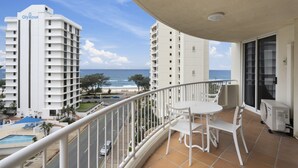 Un balcon avec vue sur la plage et l’océan, des meubles blancs et un espace piscine.