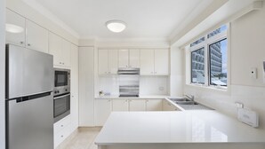 Une cuisine moderne avec des meubles blancs, des appareils en acier inoxydable et une grande fenêtre offrant une vue sur l’extérieur.
