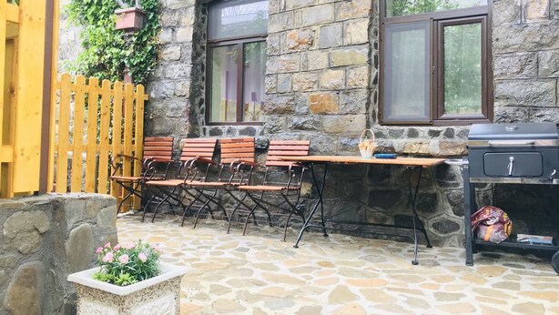 An outdoor patio with stone flooring, wooden benches, a grill, and a wooden fence. - Apartment Carol (Sinaia)
