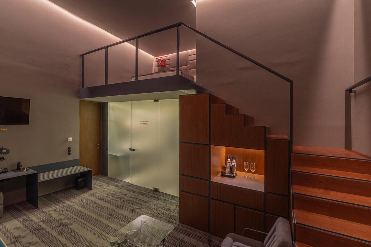 A modern loft-style room with a mezzanine, a wooden staircase, and a seating area with a coffee table.