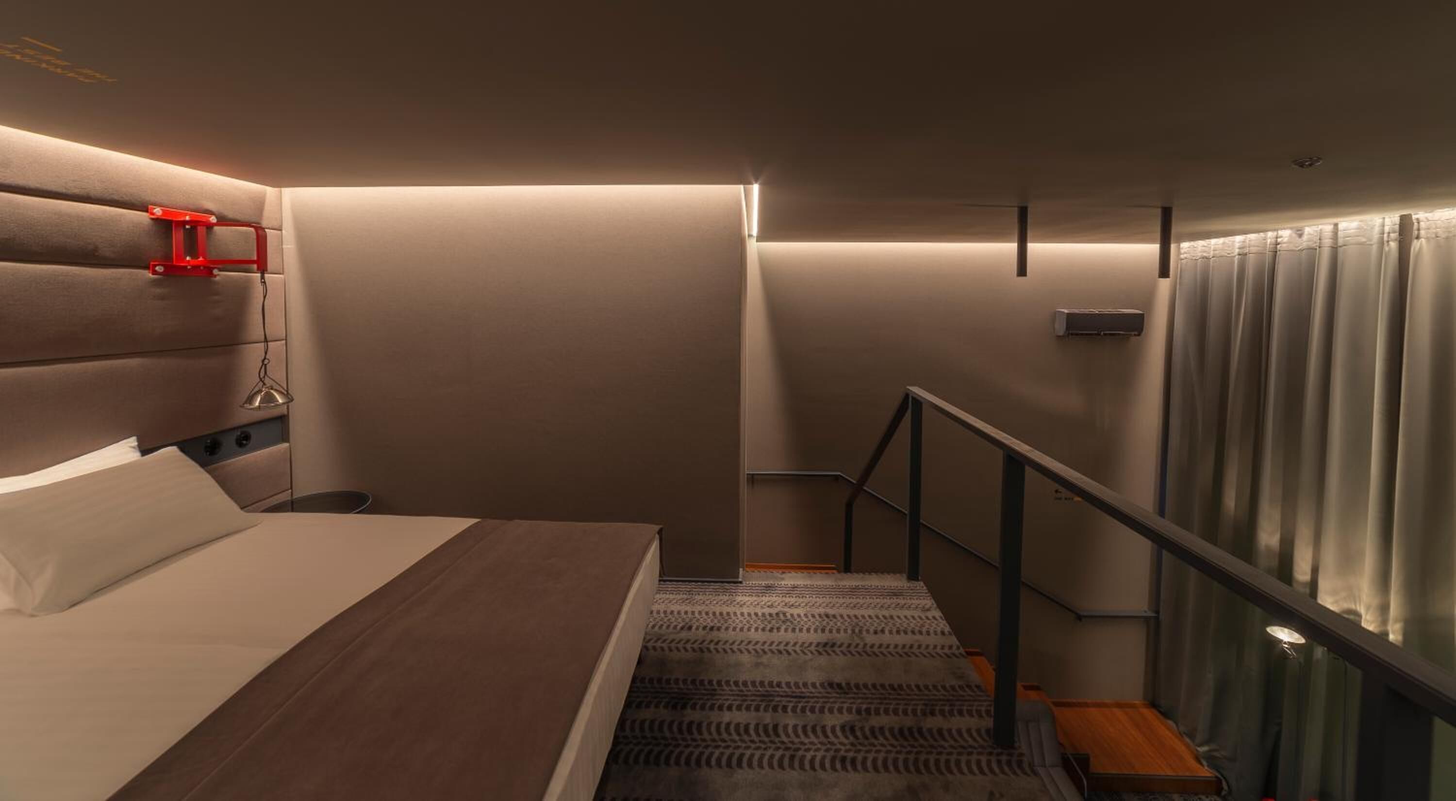 A hotel room with a bed, a headboard, a staircase, and a window with curtains.