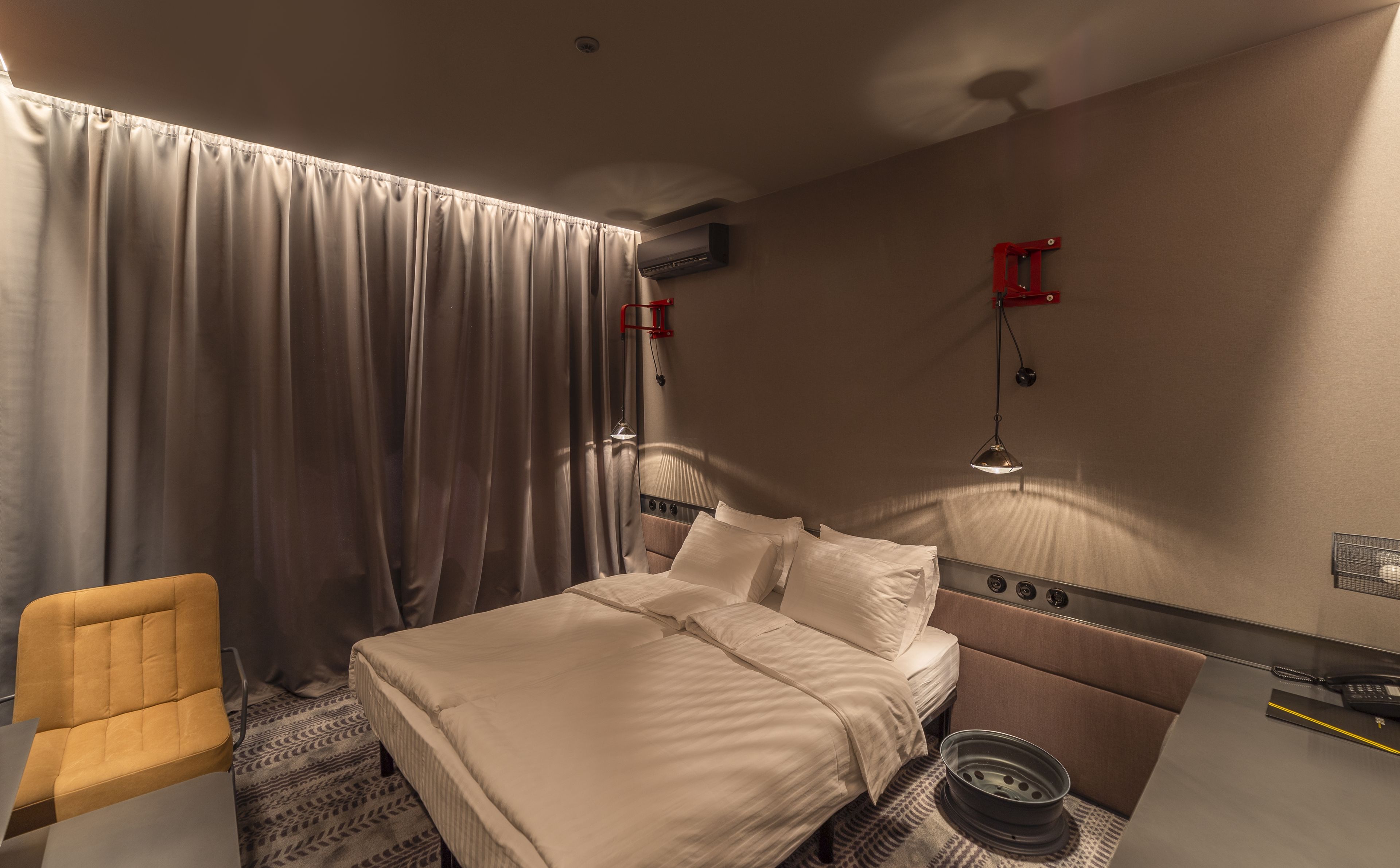 Una habitación de hotel con una cama, una silla, un escritorio, una lámpara y un ventilador de techo.
