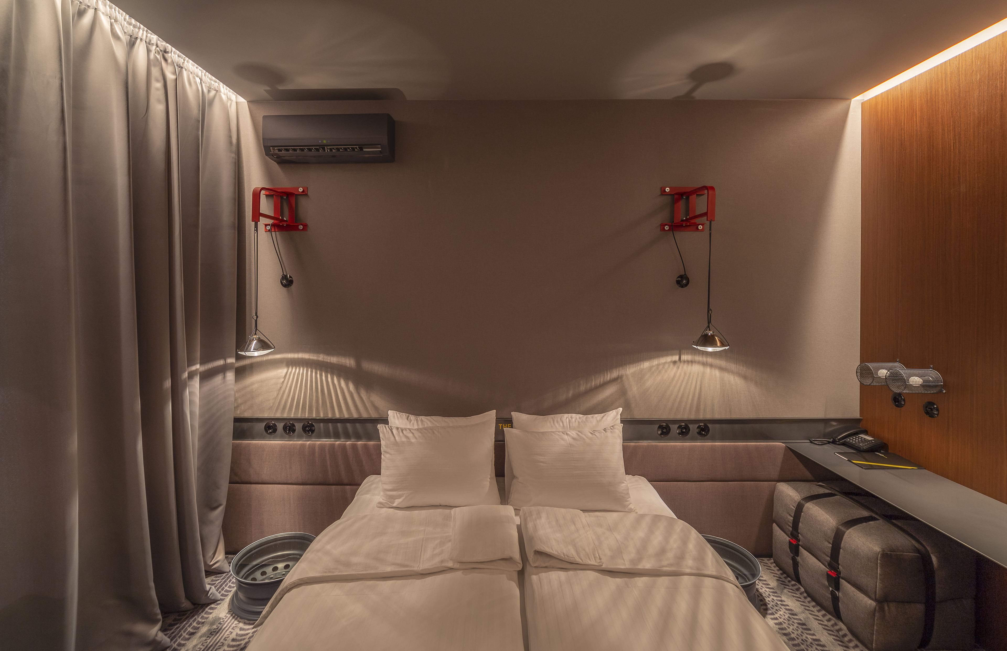 Quarto compacto e bem iluminado, com cama, mesas de cabeceira e um pequeno espaço para escritório.