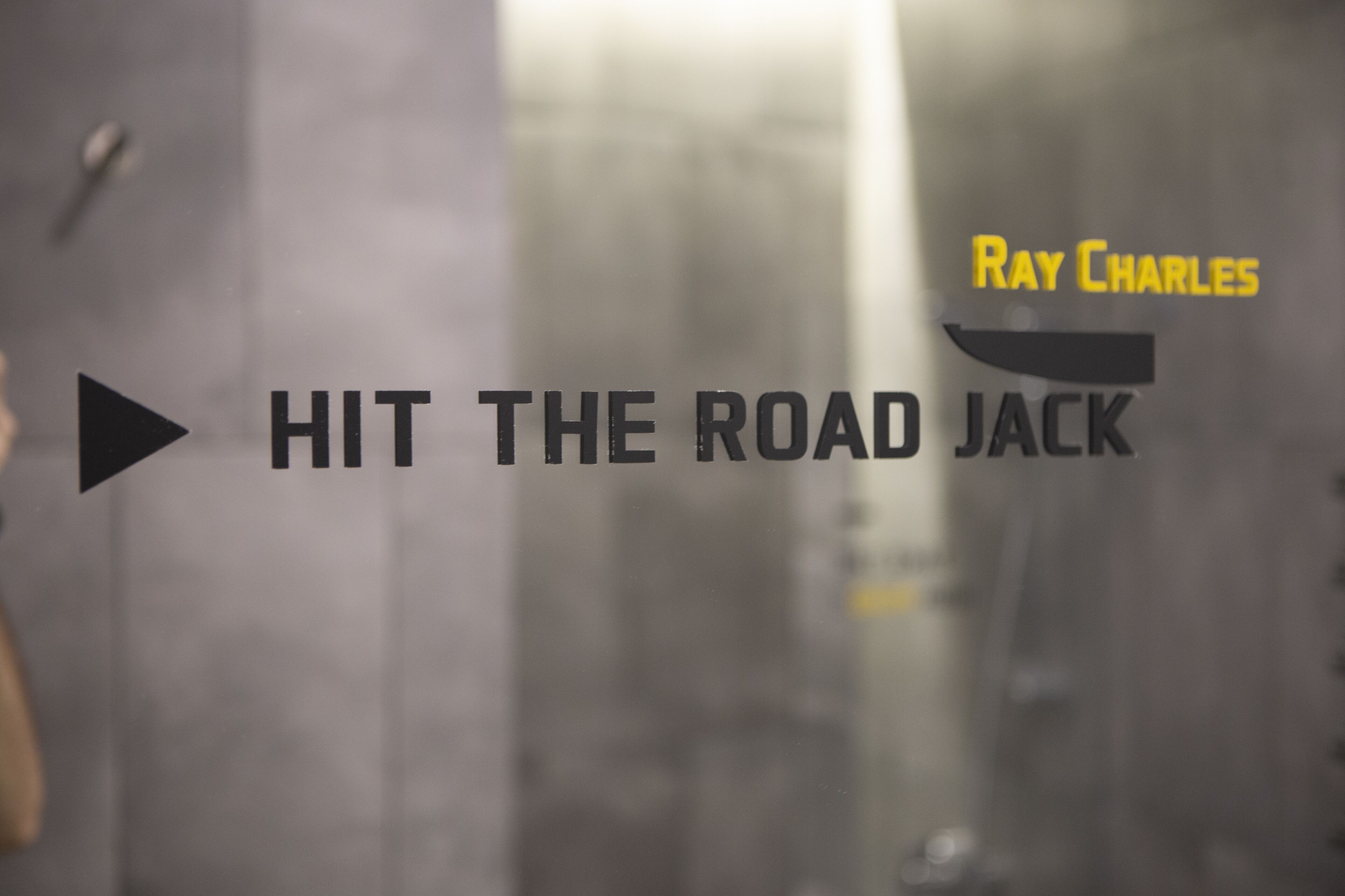 Fundo desfocado com o texto 'HIT THE ROAD JACK' e 'Ray Charles' visíveis.