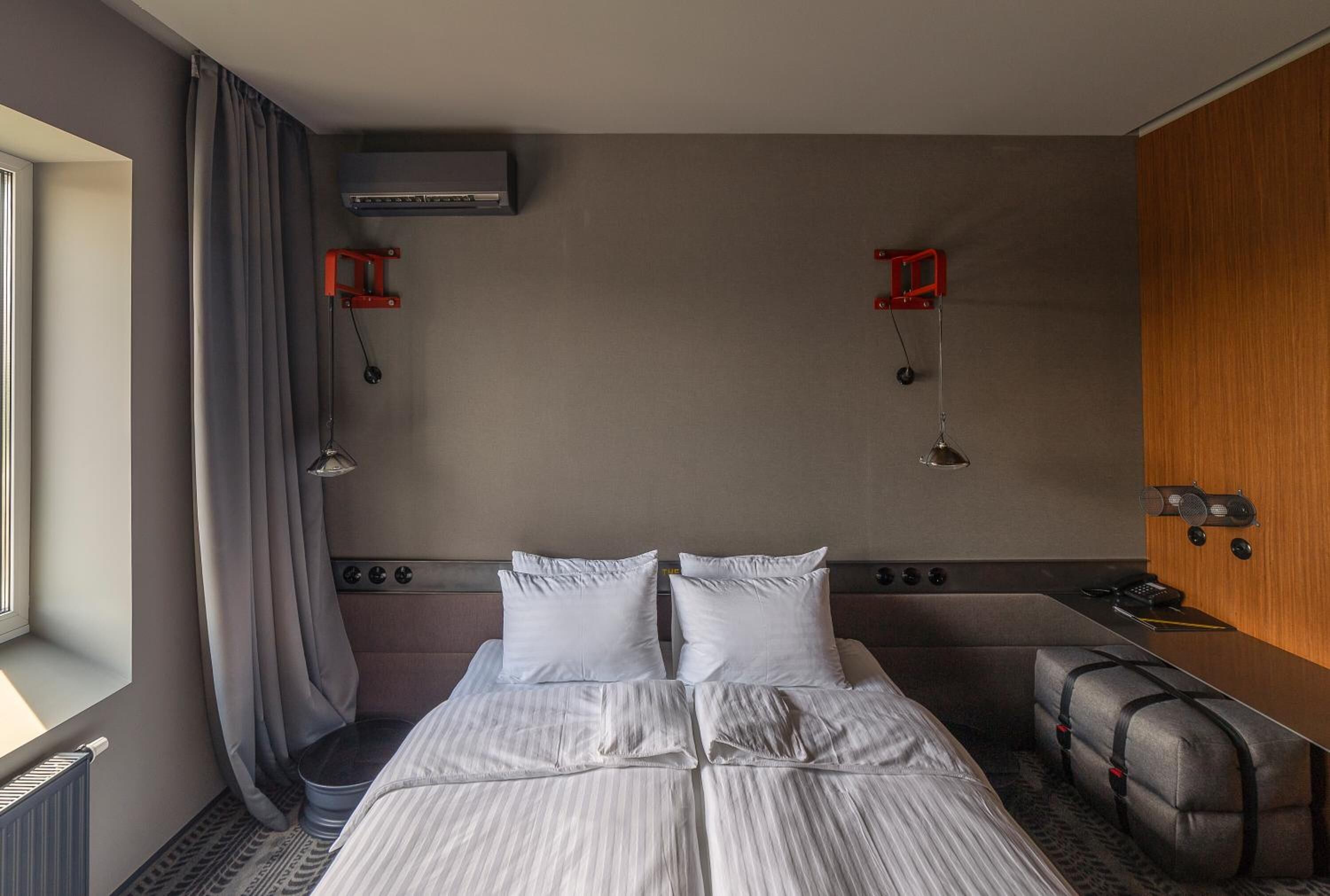 Habitación de hotel con una cama grande, un escritorio pequeño, una silla, una ventana con cortinas y aire acondicionado de pared.