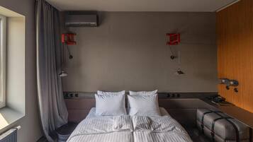 Habitación de hotel con una cama grande, un escritorio pequeño, una silla, una ventana con cortinas y aire acondicionado de pared.