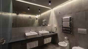 Un baño moderno con dos lavamanos, un bidé y un inodoro. Hay toallas colgadas en la pared y un espejo sobre los lavamanos.