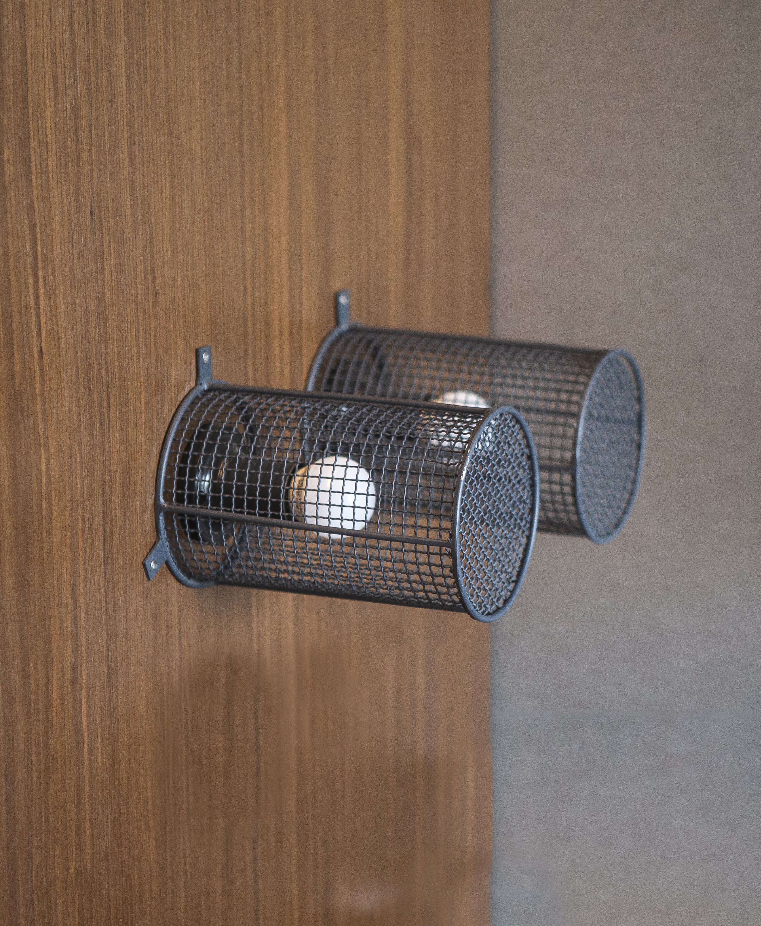 Two cylindrical metal mesh objects mounted on a wooden surface.