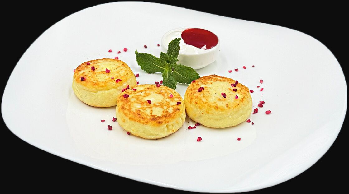 A white plate with three small pastries, a small bowl of red sauce, and a mint leaf garnish.