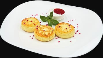 A white plate with three small pastries, a small bowl of red sauce, and a mint leaf garnish.