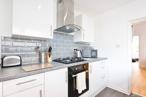 A modern kitchen with white cabinets, a gas stove, a microwave, and a toaster. - Amazing Views of the City (Swansea)