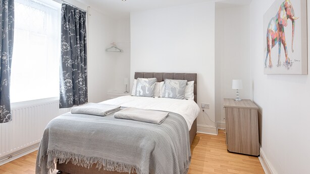 Ein Schlafzimmer mit einem Bett, einem Nachttisch, einer Lampe und einem Bild an der Wand.