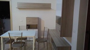 A dining area with a white table and four chairs, a wooden cabinet, and a TV mounted on the wall. - B&B Tatti (Nughedu Santa Vittoria)