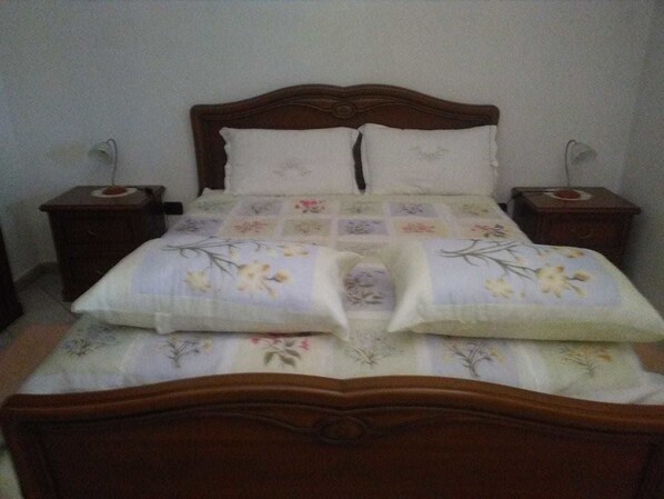 Un dormitorio con cabecera de cama de madera, dos mesitas de noche y una colcha con estampado floral.